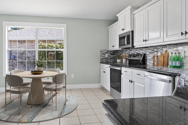 kitchen with decorative backsplash, stainless steel appliances, dark stone countertops, white cabinets, and light tile patterned flooring