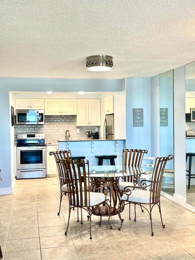 kitchen with light tile patterned floors, a textured ceiling, appliances with stainless steel finishes, and tasteful backsplash