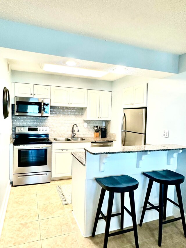 kitchen featuring white cabinetry, sink, dark stone counters, and appliances with stainless steel finishes