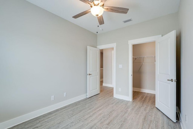 unfurnished bedroom featuring ceiling fan, a closet, a spacious closet, and light wood-type flooring