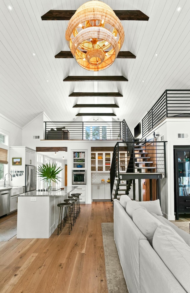 living room with wood ceiling, beam ceiling, an inviting chandelier, light hardwood / wood-style flooring, and high vaulted ceiling