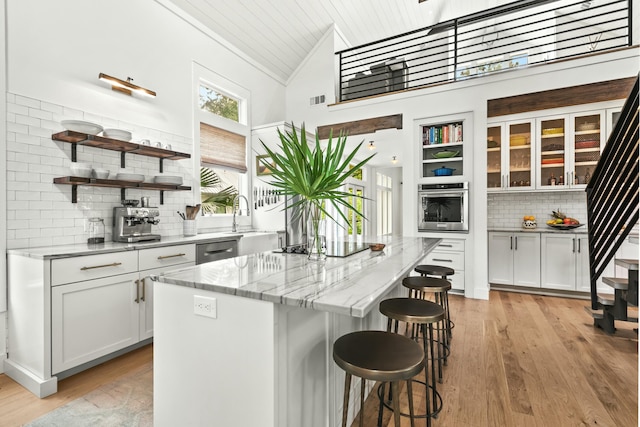 kitchen featuring a towering ceiling, stainless steel appliances, white cabinetry, and a kitchen island