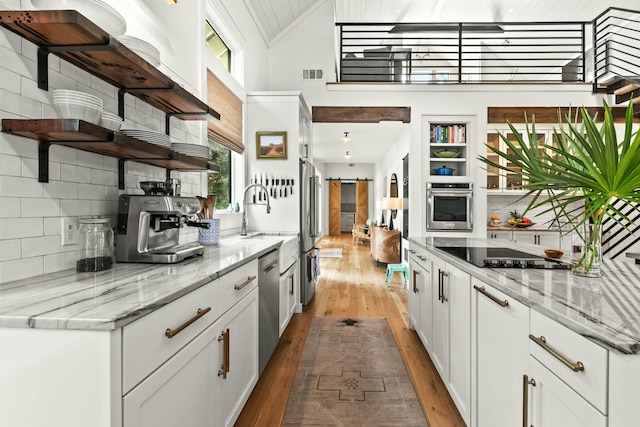 kitchen featuring light stone countertops, appliances with stainless steel finishes, light wood-type flooring, a barn door, and white cabinetry