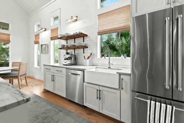 kitchen featuring light stone countertops, sink, stainless steel appliances, hardwood / wood-style floors, and vaulted ceiling