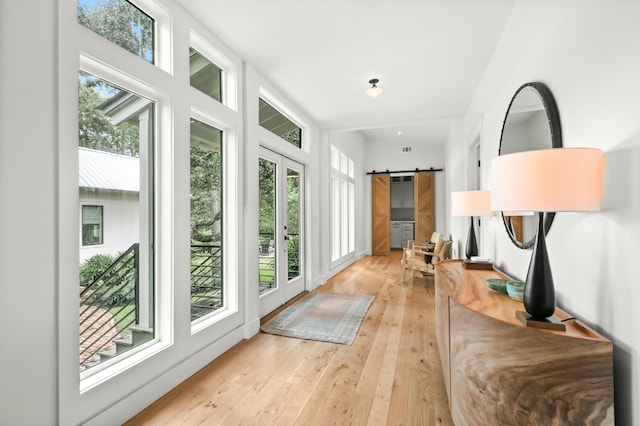 hallway with french doors, a barn door, and light hardwood / wood-style floors