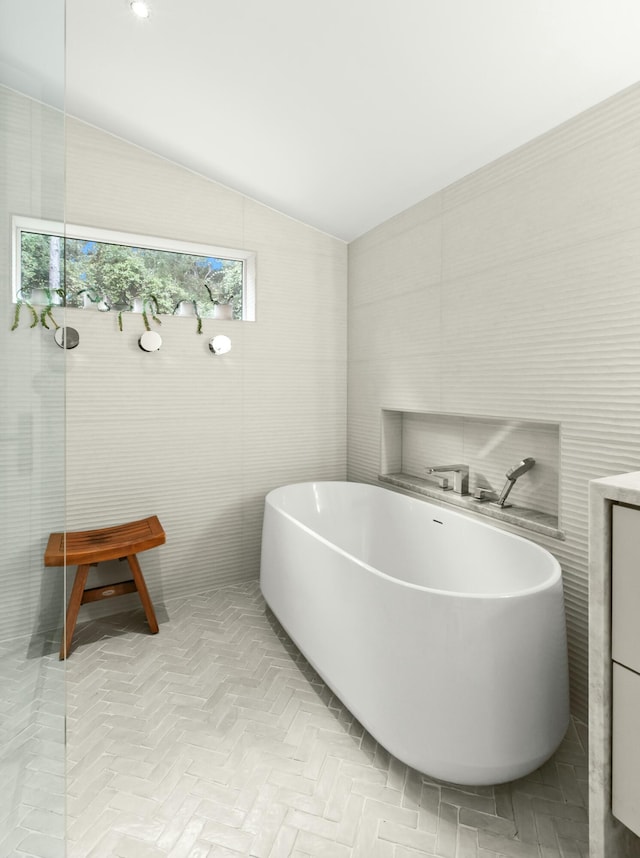 bathroom featuring vanity, a tub to relax in, vaulted ceiling, and tile walls