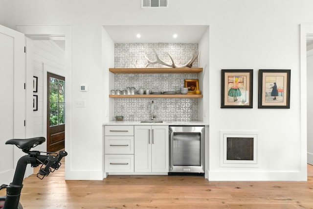 bar with white cabinetry, sink, beverage cooler, decorative backsplash, and light wood-type flooring