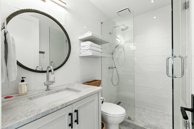 bathroom with a shower with door, vanity, tile walls, and toilet