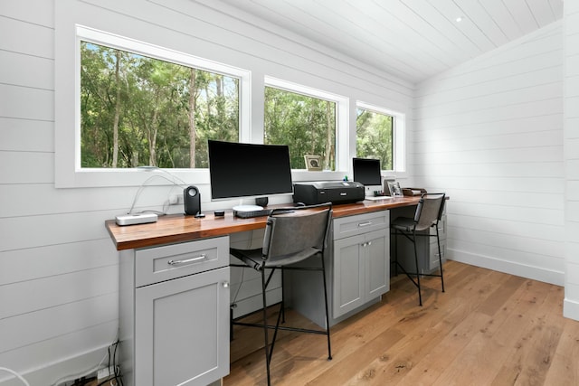 office featuring a wealth of natural light, light hardwood / wood-style flooring, lofted ceiling, and wooden walls