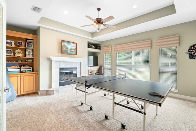 game room with light carpet, a raised ceiling, ceiling fan, and a tiled fireplace