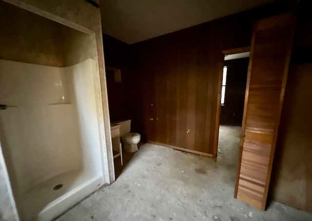 bathroom with wood walls, a shower, concrete flooring, and toilet