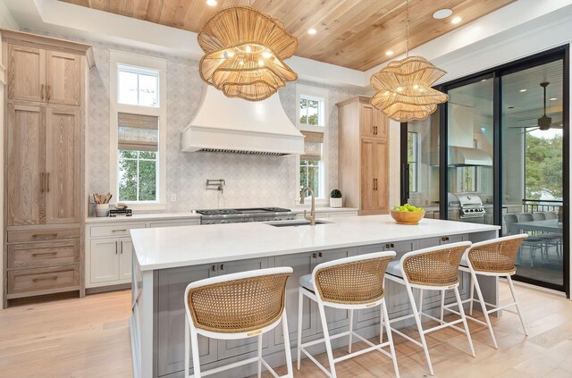 kitchen with light brown cabinetry, light hardwood / wood-style flooring, a kitchen island with sink, and wood ceiling