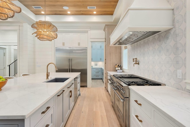 kitchen featuring high end appliances, sink, decorative light fixtures, custom exhaust hood, and light wood-type flooring