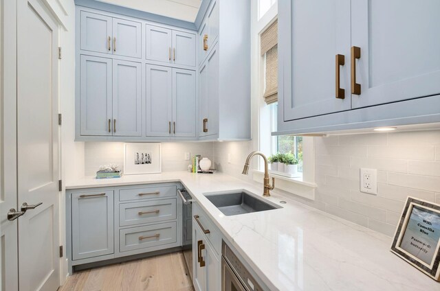 kitchen with dishwasher, backsplash, sink, light hardwood / wood-style flooring, and light stone countertops