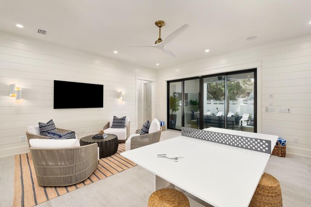 living room featuring ceiling fan, light hardwood / wood-style flooring, and wood walls