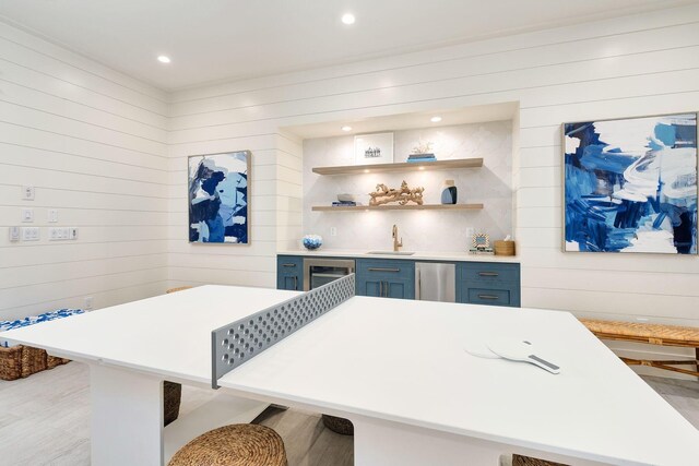 kitchen with sink, a kitchen breakfast bar, blue cabinets, light hardwood / wood-style floors, and wooden walls