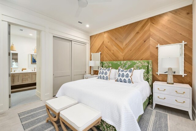 bedroom featuring ensuite bath, ceiling fan, a closet, and wood walls