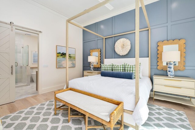 bedroom with a barn door, light wood-type flooring, crown molding, and connected bathroom