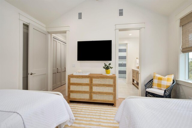 bedroom featuring light wood-type flooring, lofted ceiling, connected bathroom, and a closet