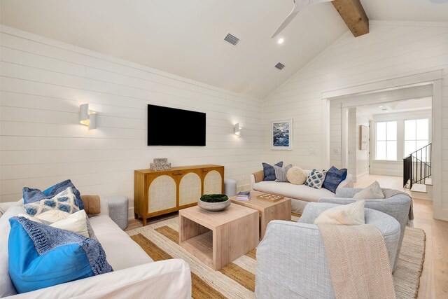 living room featuring high vaulted ceiling, wooden walls, ceiling fan, light wood-type flooring, and beam ceiling