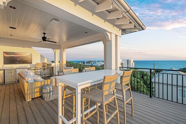 deck at dusk featuring area for grilling, ceiling fan, and a water view