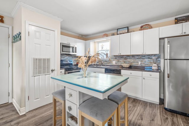 kitchen featuring white cabinets, backsplash, appliances with stainless steel finishes, and hardwood / wood-style floors