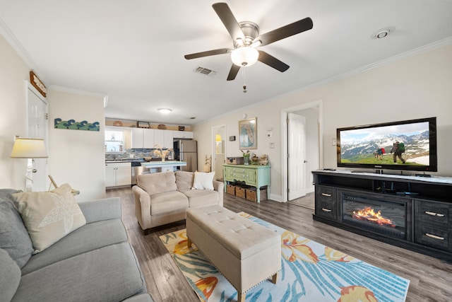 living room featuring hardwood / wood-style flooring, ceiling fan, and crown molding