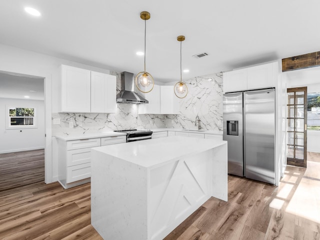 kitchen featuring a healthy amount of sunlight, wall chimney range hood, stainless steel appliances, and white cabinetry