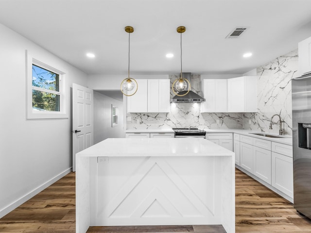 kitchen with white cabinets, sink, wall chimney exhaust hood, decorative light fixtures, and stainless steel appliances