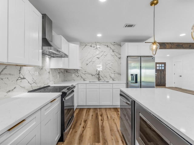 kitchen featuring decorative light fixtures, white cabinetry, wall chimney range hood, and stainless steel appliances