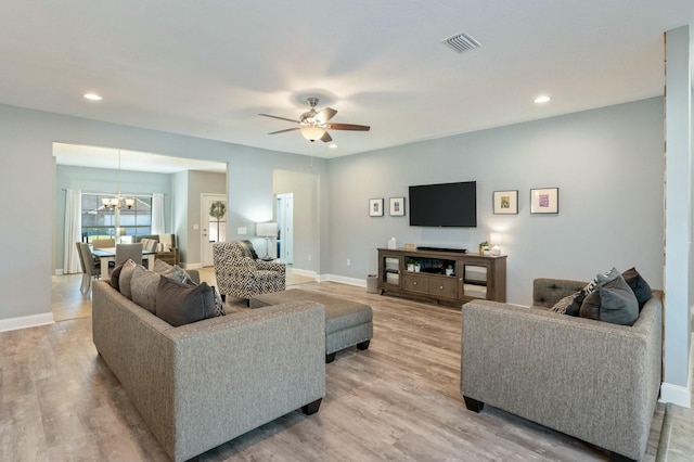 living room featuring ceiling fan with notable chandelier and light wood-type flooring