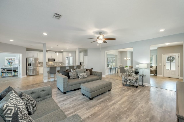 living room featuring ceiling fan with notable chandelier and light hardwood / wood-style floors