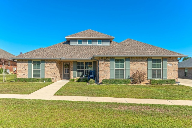 view of front of home with brick siding, roof with shingles, and a front yard