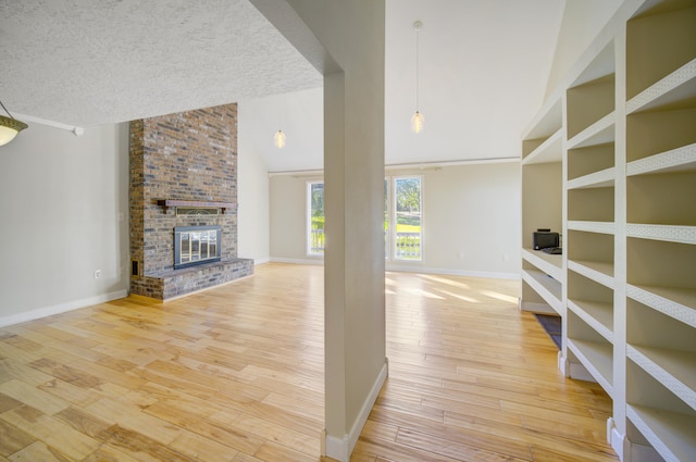 unfurnished living room with a textured ceiling, hardwood / wood-style flooring, a brick fireplace, and high vaulted ceiling