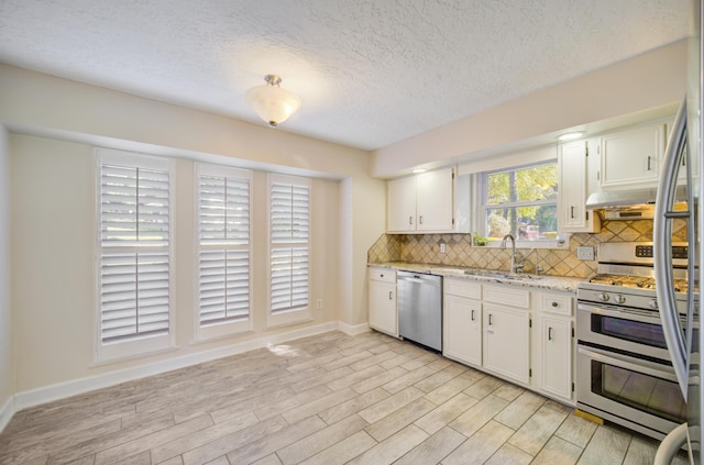 kitchen featuring appliances with stainless steel finishes, light stone counters, sink, light hardwood / wood-style floors, and white cabinetry