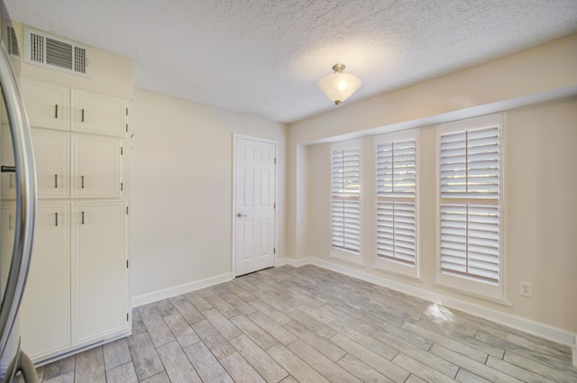 unfurnished room featuring a textured ceiling and light hardwood / wood-style flooring