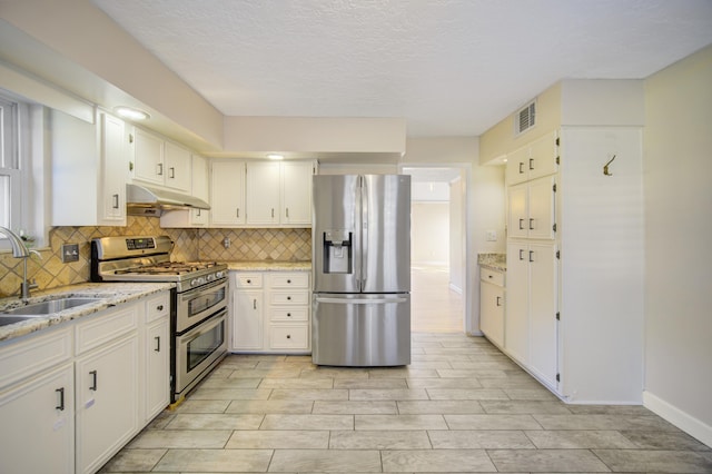 kitchen with white cabinets, sink, light stone countertops, a textured ceiling, and stainless steel appliances