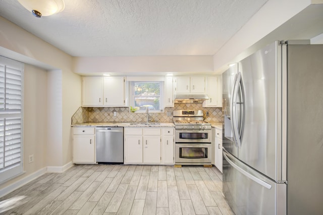 kitchen with appliances with stainless steel finishes, light stone counters, sink, white cabinets, and light hardwood / wood-style floors