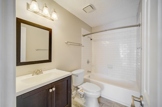 full bathroom with vanity, toilet, a textured ceiling, and tiled shower / bath combo