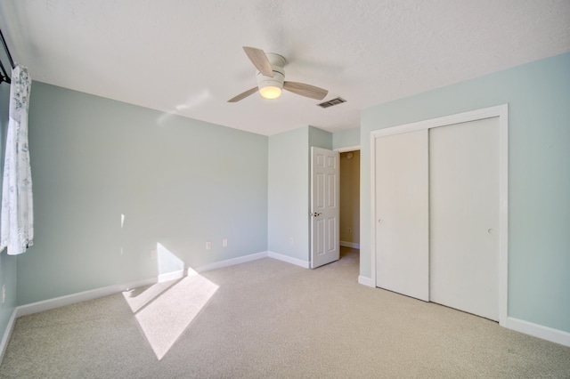 unfurnished bedroom with ceiling fan, light colored carpet, a textured ceiling, and a closet