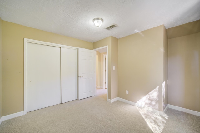 unfurnished bedroom featuring light carpet, a closet, and a textured ceiling