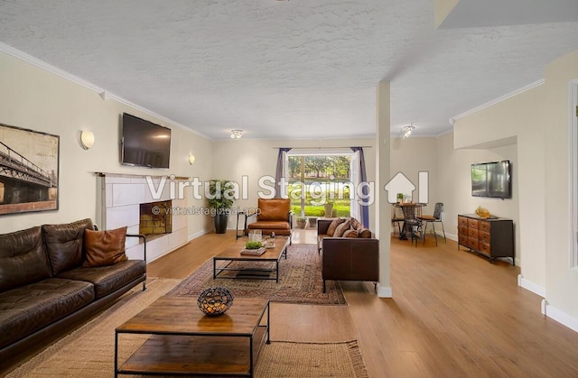 living room with a tile fireplace, a textured ceiling, crown molding, and wood finished floors