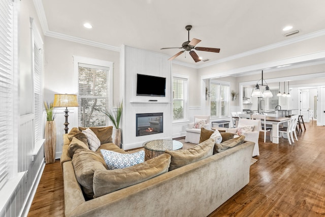 living room with a fireplace, ceiling fan, crown molding, and dark wood-type flooring