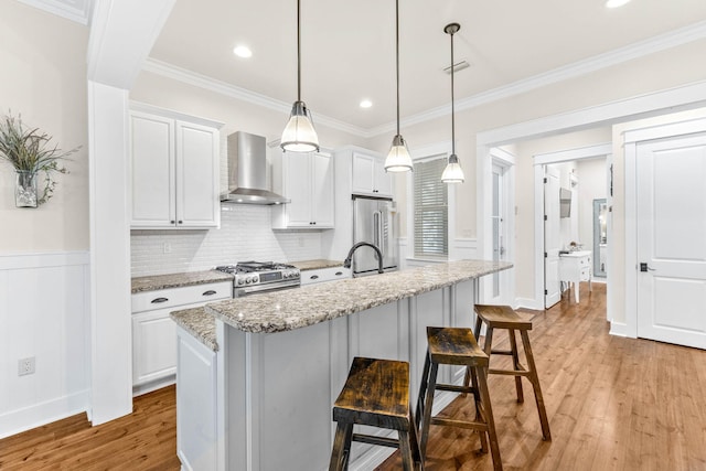 kitchen with appliances with stainless steel finishes, light wood-type flooring, light stone counters, wall chimney range hood, and white cabinetry