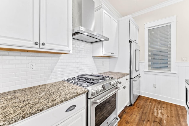 kitchen with light stone countertops, white cabinets, high quality appliances, and wall chimney range hood