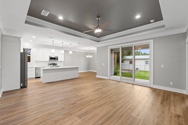 unfurnished living room featuring ceiling fan with notable chandelier, light wood-type flooring, a tray ceiling, and ornamental molding