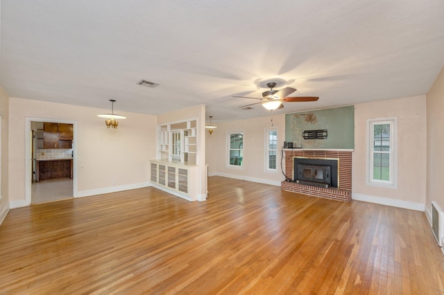 unfurnished living room featuring ceiling fan, light hardwood / wood-style floors, a wealth of natural light, and a fireplace