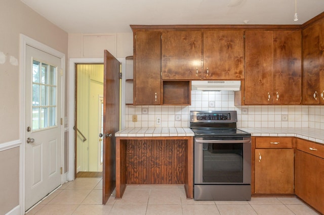 kitchen featuring electric range, light tile patterned floors, tasteful backsplash, and tile counters