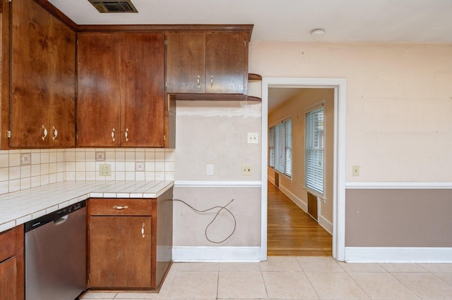 kitchen with stainless steel dishwasher, light tile patterned flooring, tile countertops, and backsplash