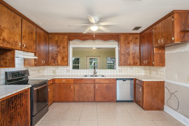 kitchen with stainless steel appliances, light tile patterned floors, ceiling fan, tile countertops, and sink